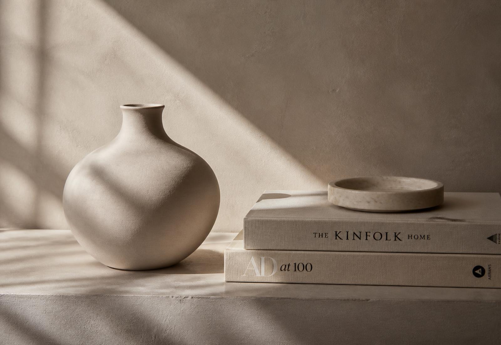 Ceramic vessel beside linen-bound books in soft daylight